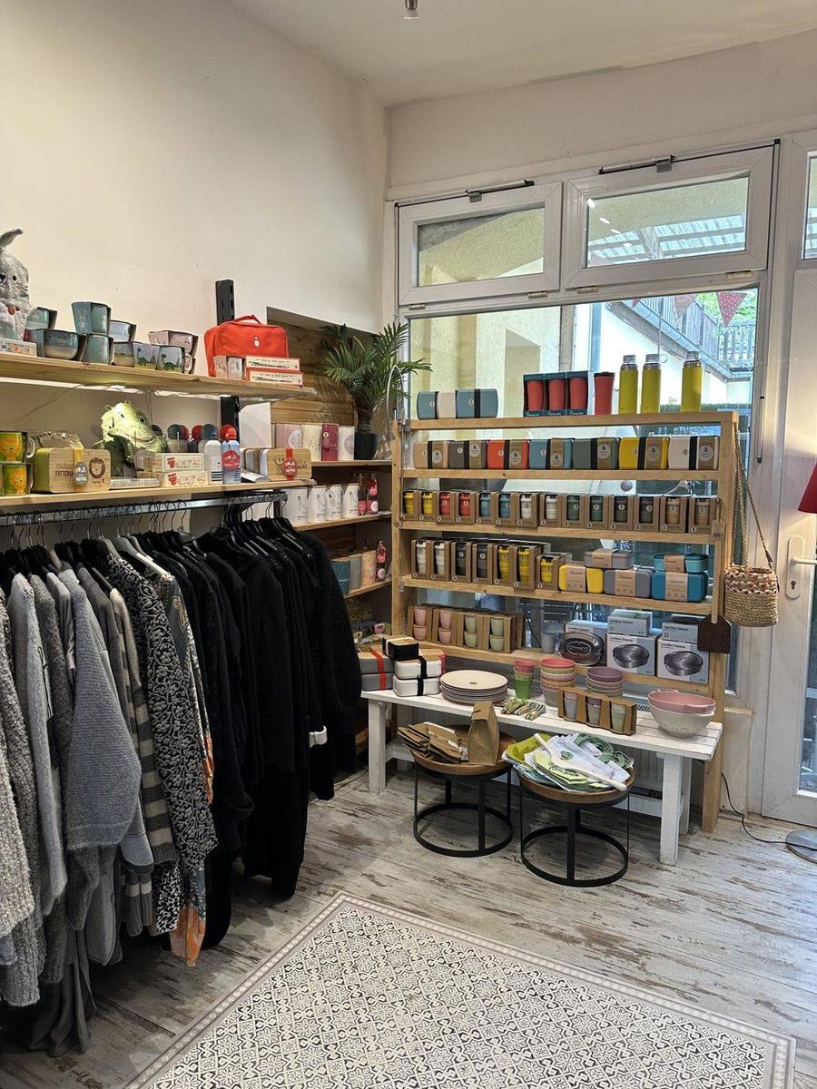 Ecke des Ladens mit Regalen voller Geschirr und dunklen Kleiderstangen